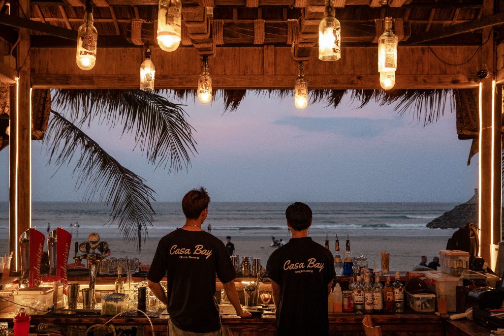 Two Casa Bay bartenders standing at the bar overlooking the ocean at dusk