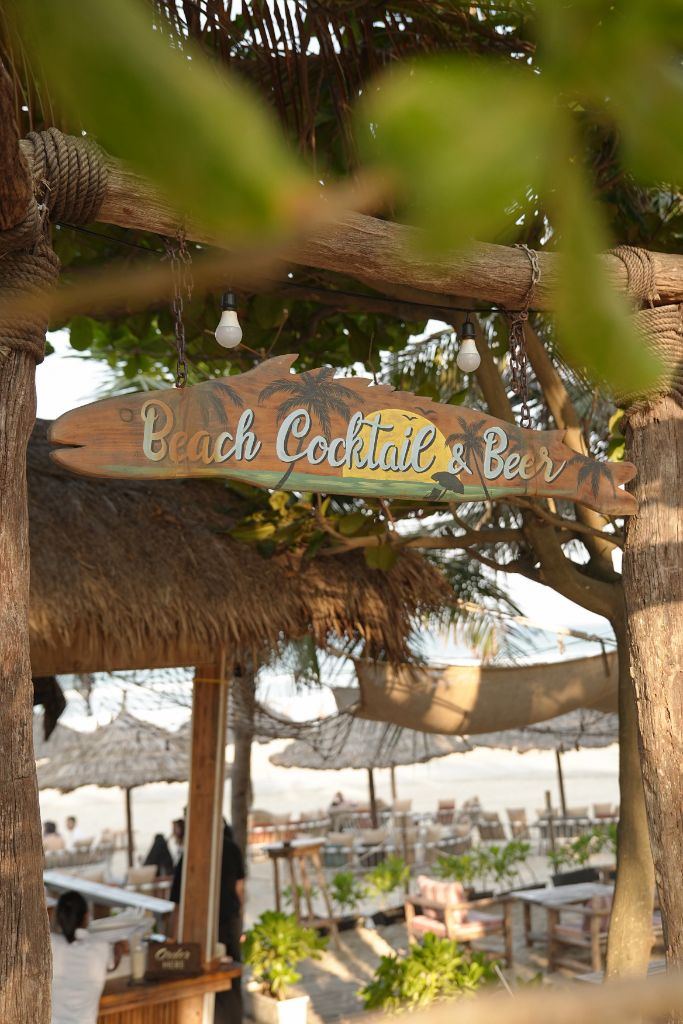 Beach Cocktail & Beer wooden surfboard sign hanging between palm trees