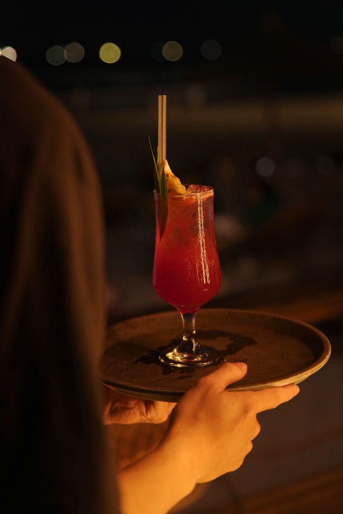 Signature red cocktail served on a wooden tray at Casa Bay at night