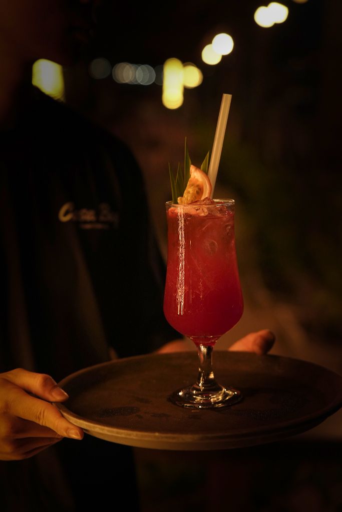 Casa Bay bartender holding a red cocktail on a tray under bokeh lights