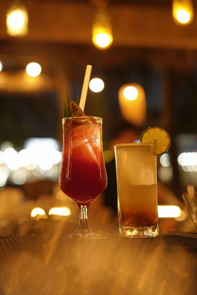 Two cocktails — a red sling and a golden drink — on the bar counter at Casa Bay